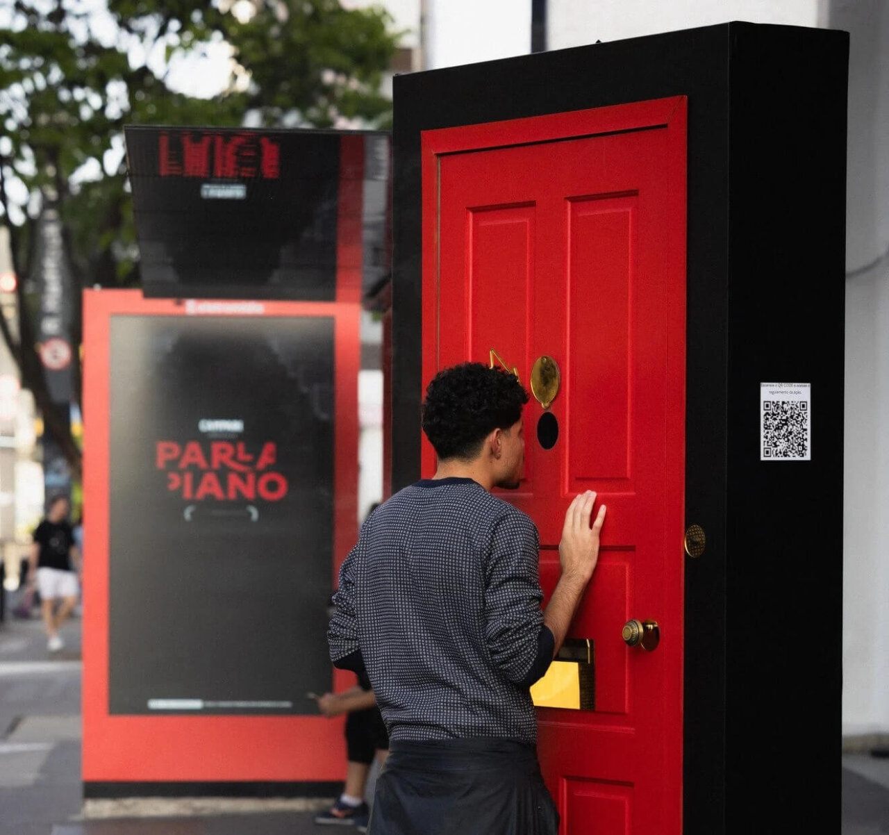 Pessoas interagindo com a porta vermelha do Parla Piano na Avenida Paulista.