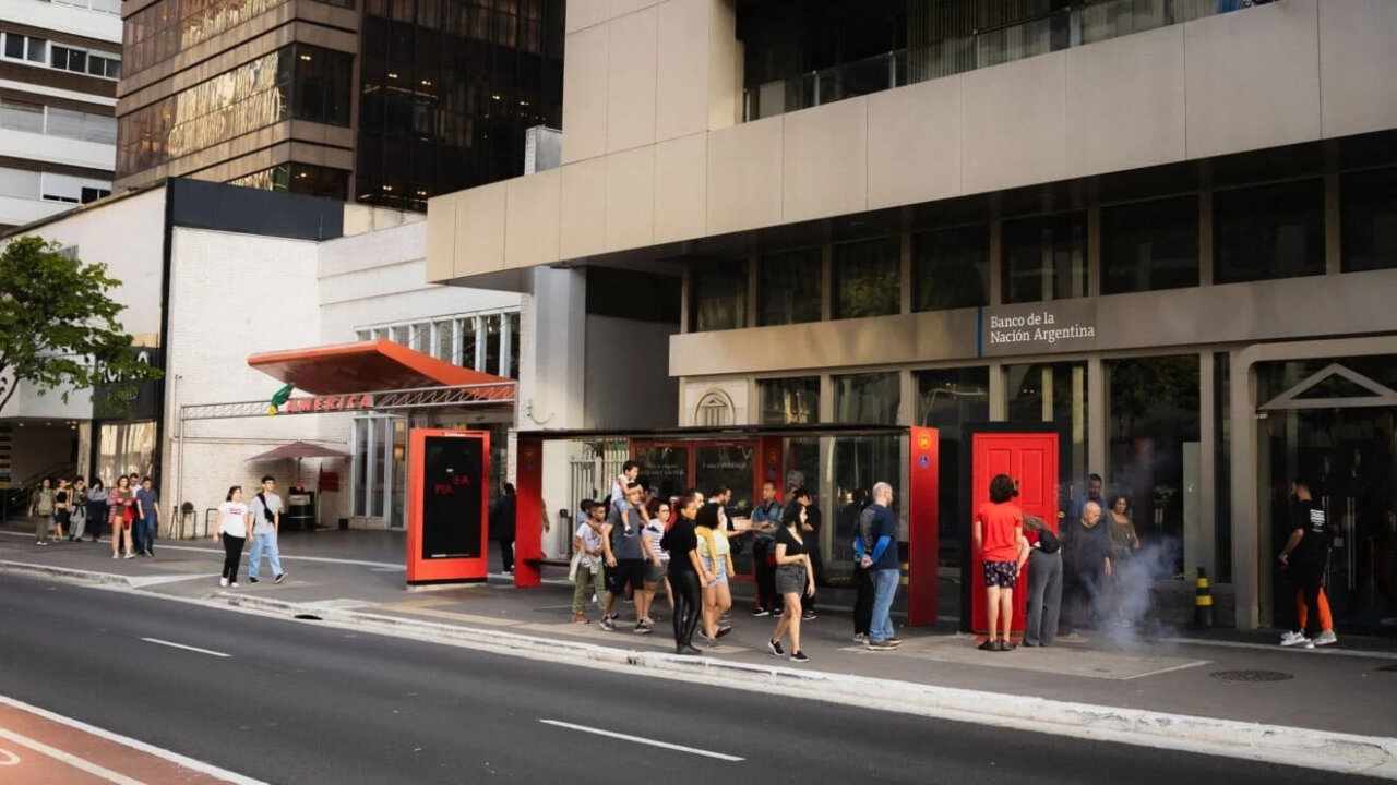 Pessoas interagindo com a porta vermelha do Parla Piano na Avenida Paulista.