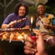 Pessoa acendendo uma vela de aniversário com um isqueiro BIC, rodeada por amigos sorrindo em uma comemoração intimista, simbolizando conexão emocional e momentos especiais da vida cotidiana.