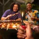 Pessoa acendendo uma vela de aniversário com um isqueiro BIC, rodeada por amigos sorrindo em uma comemoração intimista, simbolizando conexão emocional e momentos especiais da vida cotidiana.