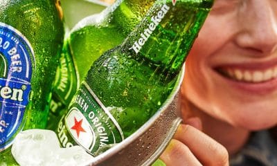 Fotografia conceitual de rótulos e embalagens inspiradas na paleta verde Heineken, com destaque para uma estrela vermelha estilizada ao lado do wordmark, representando a evolução do logo ao longo do tempo.