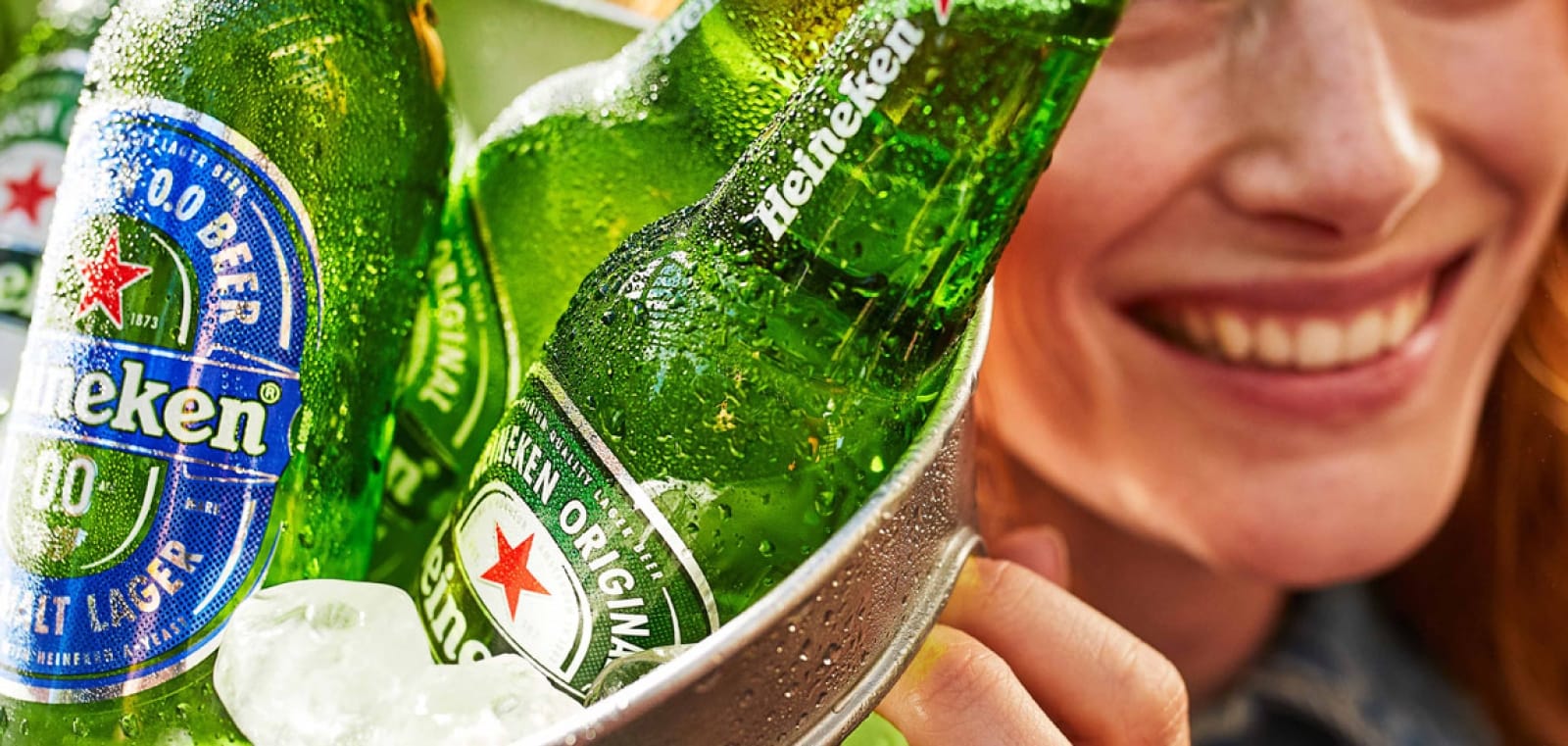 Fotografia conceitual de rótulos e embalagens inspiradas na paleta verde Heineken, com destaque para uma estrela vermelha estilizada ao lado do wordmark, representando a evolução do logo ao longo do tempo.