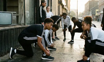 Atletas se preparando para treinar em ambiente urbano, com roupas esportivas de listras brancas, em contraste com uma televisão antiga desligada ao fundo, simbolizando a transição da adidas da TV tradicional para o digital. Adidas parou de investir em TV