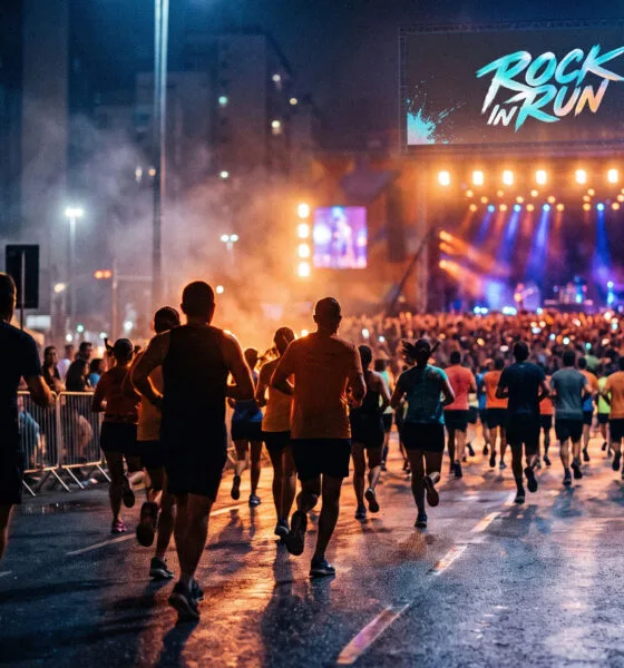 Corredores durante corrida noturna organizada por marca de entretenimento, com show ao fundo